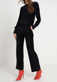 Svart velour-matching set med långärmad topp med asymmetrisk design och vida byxor, parat med klarröda högklackade stövlar.