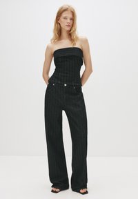 Top fără bretele din denim negru cu dungi verticale, asortat cu pantaloni drepti din denim negru, cu talie înaltă. Textură netedă, hardware minim.