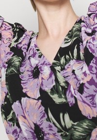 Květinové šaty s velkými fialovými a broskvovými květy na černém pozadí. Vyrobené z měkké látky s překříženým designem a krátkými nabíranými rukávy.