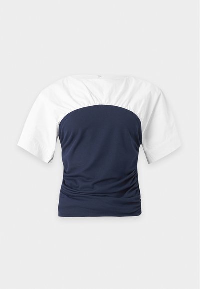 Chemise à manches courtes avec manches blanches et corsage bleu marine ajusté, vue de dos sur un fond clair uni.
