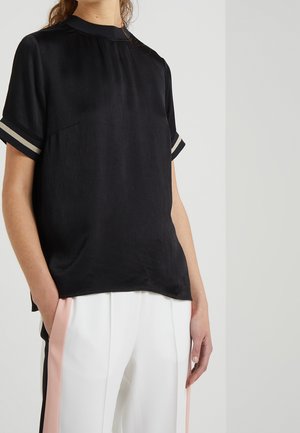 Personne portant un haut noir à manches courtes avec des poignets rayés et un pantalon blanc avec des bandes latérales verticales roses et noires.