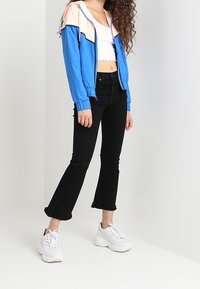 Ljust blå och persikofärgad zip-up jacka, vit crop top, svarta utsvängda jeans och klumpiga vita sneakers. Slät tyg och fransade fållar.