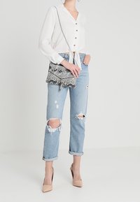 Harmaa-mustakuviollinen olkalaukku ketjusangalla, yhdistetty valkoiseen nappipaitaan ja vaaleansinisiin kulutettuihin farkkuihin.