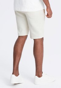 Lys beige bomulds shorts med en regulær pasform, sidelommer og en glat tekstur, parret med hvide sneakers.