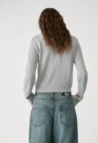 Gray knitted sweater with long sleeves, ribbed cuffs, and hem, paired with high-waisted light blue denim jeans featuring dual back pockets.