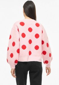 Roosa kampsun punaste täpikestega, valmistatud karvasest materjalist, lõdva istumise ja õhupallist varrukatega. Äär on lühendatud.