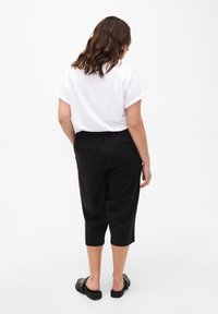 Pantalons noirs courts avec une taille élastique et des poches latérales, associés à un t-shirt blanc à manches courtes et des chaussures noires à enfiler.