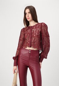 Burgundy lace cropped blouse with long puff sleeves and button closure, paired with matching high-waisted leather pants, smooth texture.