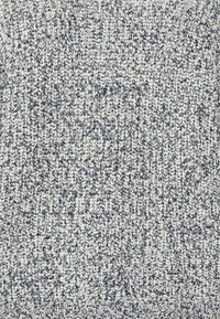 Stickad tyg i nyanser av blått och vitt, med ett strukturerat mönster med varierande tjocklekar, vilket ger ett mjukt utseende.