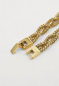 Gullkjede med sammenflettede lenker, med to distinkte firkantede låser; den ene er gravert med "Guess" og har et strukturert mønster.