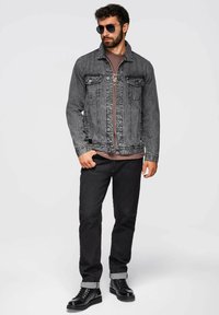 Giacca in denim nera, t-shirt grigia, jeans neri con risvolto, e stivali neri. Gli accessori includono occhiali da sole. Design semplice e casual.