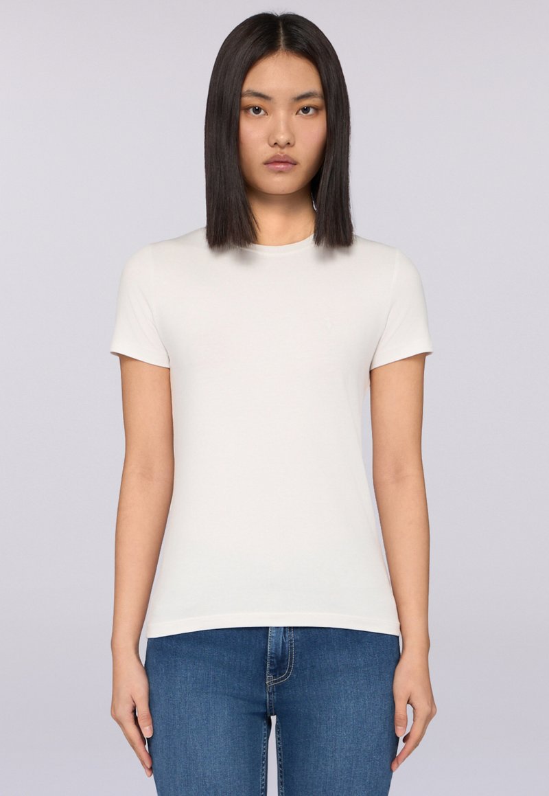 Bílý krátký rukáv tričko ve slim fit designu, vyrobené z hladkého, lehkého materiálu. Sestaveno s modrými džíny, které prezentují jednoduchý, klasický vzhled.