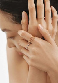 Tres anillos en los dedos: uno dorado con un diseño elegante, uno plateado con una pequeña gema azul y otro plateado con una banda texturizada.