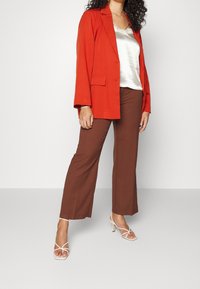 Red blazer, cream satin top, brown wide-leg pants, and white strappy heels. The blazer has a tailored fit and two front pockets.