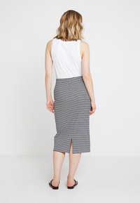 Černobílá pruhovaná midi sukně s rozparkem vzadu, spárovaná s bílým topem bez rukávů. Tkanina vypadá hladce a těsně.