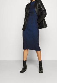 Stickad blå klänning med vertikala ränder, tillsammans med en svart läderjacka och svarta ankelstövlar, som visar upp en figurnära design och längd till mitt på vaden.