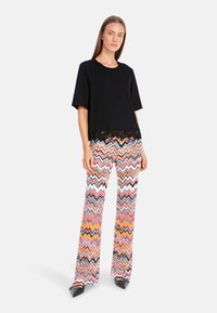 Black short-sleeve top with lace detail, paired with multicolored zigzag patterned flared pants in orange, pink, and white. Black shoes.