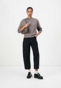 Gray oversized sweatshirt with a blue logo, black high-waisted jeans, and black chunky shoes. Also features a green crossbody bag.