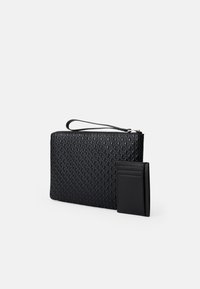 Porte-monnaie en cuir noir à motifs avec une sangle pour le poignet et un porte-cartes assorti. Surface texturée avec des détails en forme de diamant. Fermeture à glissière.