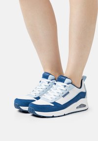 Blauwe en witte sportschoenen met een mix van mesh en suède materialen, een dikke zool en geperforeerde details met opvallende veters.