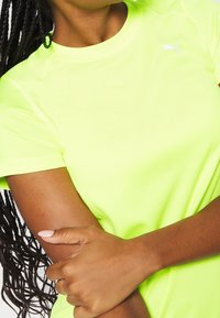 Neon žluté sportovní tričko s kulatým v ýstřihem, krátkými rukávy a malým bílým logem Puma na hrudi. Texturovaná látka.