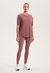 Ružová športová košeľa a zodpovedajúce legíny z hladkého, elastického materiálu. Košeľa má zaoblený lem; legíny majú zvýraznené švy.