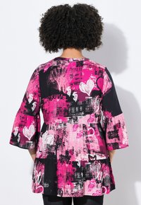 Løse ærmer top i pink og sort med grafiske prints, inklusive hjerter og dollarskilt. Letvægtsstof og en peplum-silhuet.