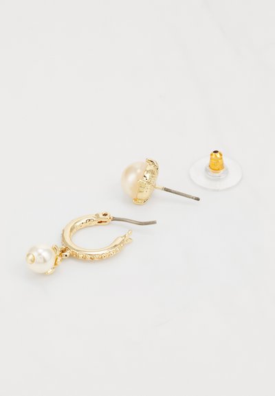 Χρυσά σκουλαρίκια σε σχήμα κρίκου με μεγάλη πέρλα και λεπτομέρειες από ρινοστάτη. Περιλαμβάνουν στήριξη με καρφί και επιπλέον διάφανη ελαστική στήριξη.