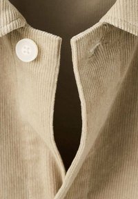 Beige corduroy shirt featuring a collared neckline, a button closure, and visible ribbed texture on the fabric.