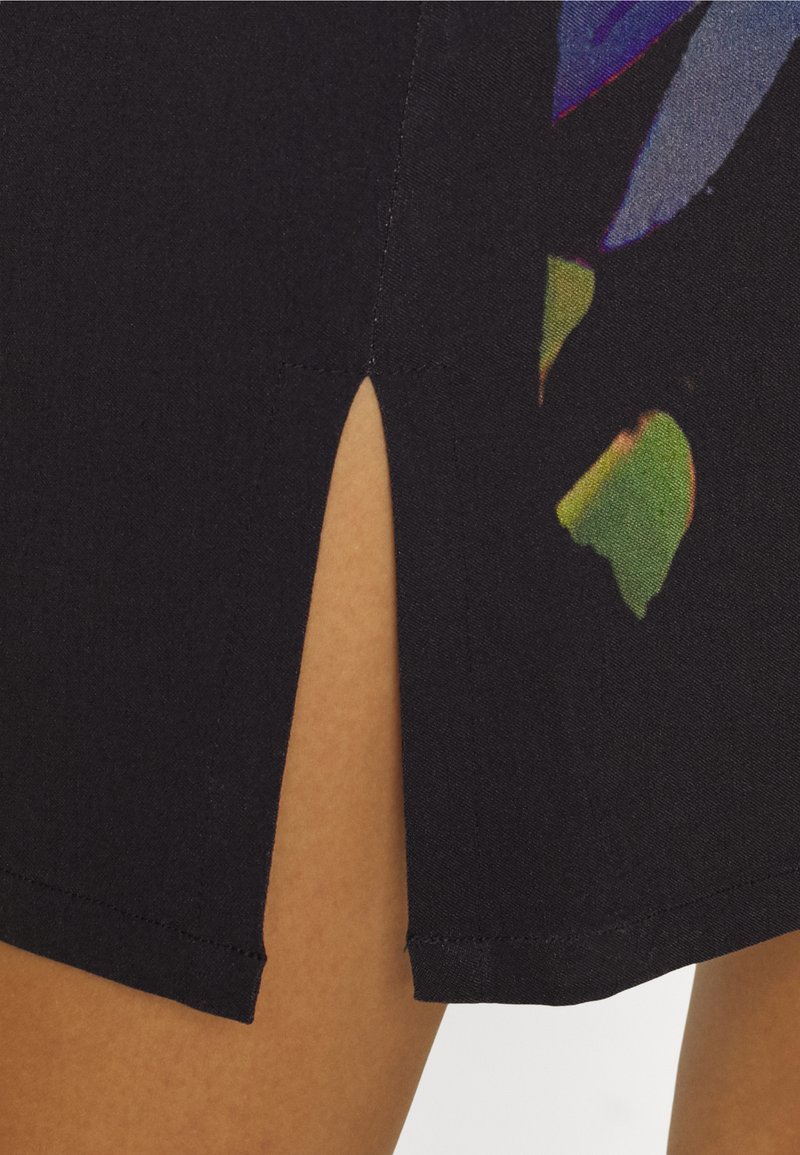Nahaufnahme eines schwarzen Rocks mit einem Schlitz vorne, der einen Teil des Beins zeigt, und einem bunten Blumenmuster am Saum.