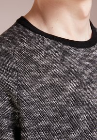 Pull en tricot noir et gris avec un motif texturé, doté d'un col rond noir côtelé et d'une finition de tissu lisse.