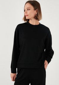 Felpa nera con colletto rotondo, maniche lunghe e vestibilità rilassata. Realizzata in un tessuto morbido, con design minimalista e senza motivi visibili.