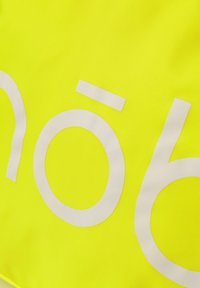 Helles gelbes Material mit großen weißen Text, glatte Textur, mit fetten Buchstaben. Das Design betont Sichtbarkeit und Einfachheit.