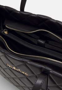 Vävd svart läderhandväska med guldfärgade detaljer, utrustad med flera blixtlåsförsedda fack och ett frontlogo som accent.