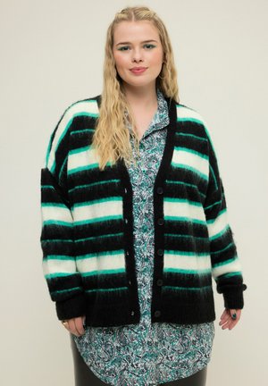 Schwarz-grün gestreifter Cardigan aus weichem, flauschigem Material mit Knöpfen, getragen über einem gemusterten grünen Paisley-Hemd. Lässige Passform.