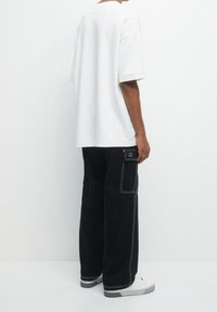 Witte oversized t-shirt met korte mouwen, gecombineerd met zwarte cargo-broeken met witte stiksels en zijzakken, gedragen met witte sneakers.