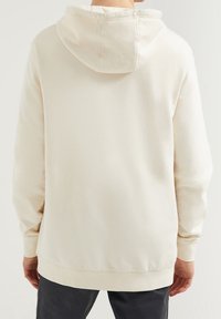 Krémově zbarvená mikina s kapucí vyrobená z měkké bavlny, s kapucí na šňůrku, klokankovou kapsou, žebrovanými lemy a volnějším střihem.