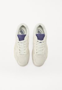Weiße Sneakers mit einem strukturierten Lederoberteil, durchbrochener Gestaltung, flachen Schnürsenkeln und lila Akzenten an der Zunge und der Markenlogo.