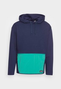 Mörkblå hoodie med teal framficka, dragsnoddshuva, långa ärmar och en liten svart logotyp patch på fickans nedersta högra del.