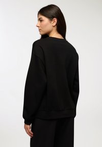 Felpa nera con collo a giro, maniche lunghe e polsini a coste, con una texture morbida e una vestibilità rilassata. Design minimalista, senza motivi.