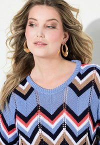 Stickad tröja med ett chevronmönster i blått, marinblått, beige och korall. Rund halsringning med öppen vävdetalj och korta ärmar.