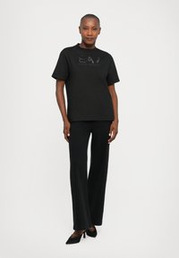 Melna kokvilnas T-kreklu ar īsām piedurknēm un apaļu kakla izgriezumu. Ar "EA7 Emporio Armani" logotipu smalkā teksturētā dizainā.