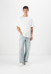 Bílá oversized tričko s krátkými rukávy, spárované s světle modrými džínami. Vyznačuje se uvolněným střihem a bílými teniskami. Jednoduchý design.