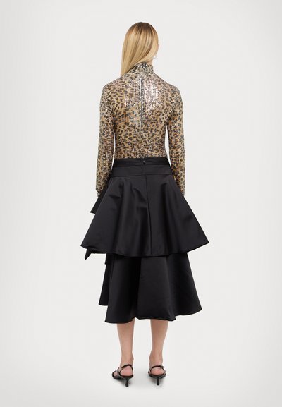 Bluză cu mâneci lungi, cu un model metalic de leopard, asortată cu o fustă midi din satin negru, cu volane. Are guler înalt și fermoar la spate.