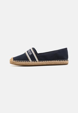 Navy blue espadrille with woven jute sole, elastic band across top featuring white and gold stripes and partial white text.