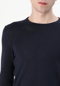 Jūras zila garām piedurknēm krekliņš ar apaļu dekoltē, izgatavots no plāna, teksturēta auduma. Tam ir šaura piegriezuma forma un smalks vītņu raksts.