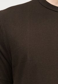 Tricou maro cu mâneci scurte, realizat dintr-un material moale și texturat. Are decolteu rotund și detalii subtile cu rebruire de-a lungul gâtului și mânecilor.