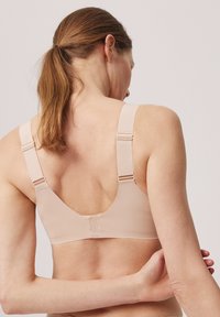 Sujetador color beige claro con tirantes anchos, tejido texturizado y cierre en la espalda. Presenta tirantes ajustables para un ajuste personalizable.