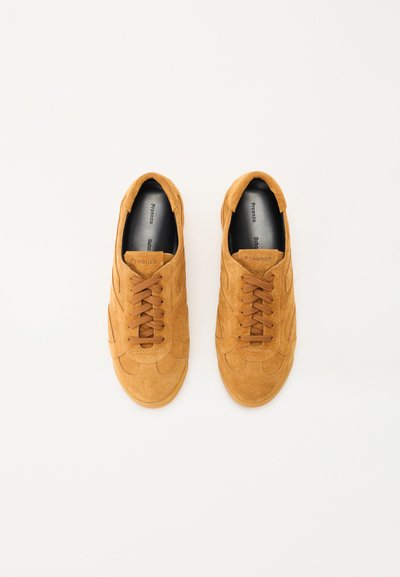 Zapatillas de ante color marrón con punta redondeada, diseño con cordones y paneles texturizados. El interior cuenta con un forro negro y un sutil logotipo en la lengüeta.