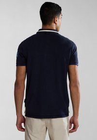 Navy modrá polo košile s klasickým designem, krátkým rukávem a kontrastním límcem. Obsahuje malé akcentové pruhy na rukávu.